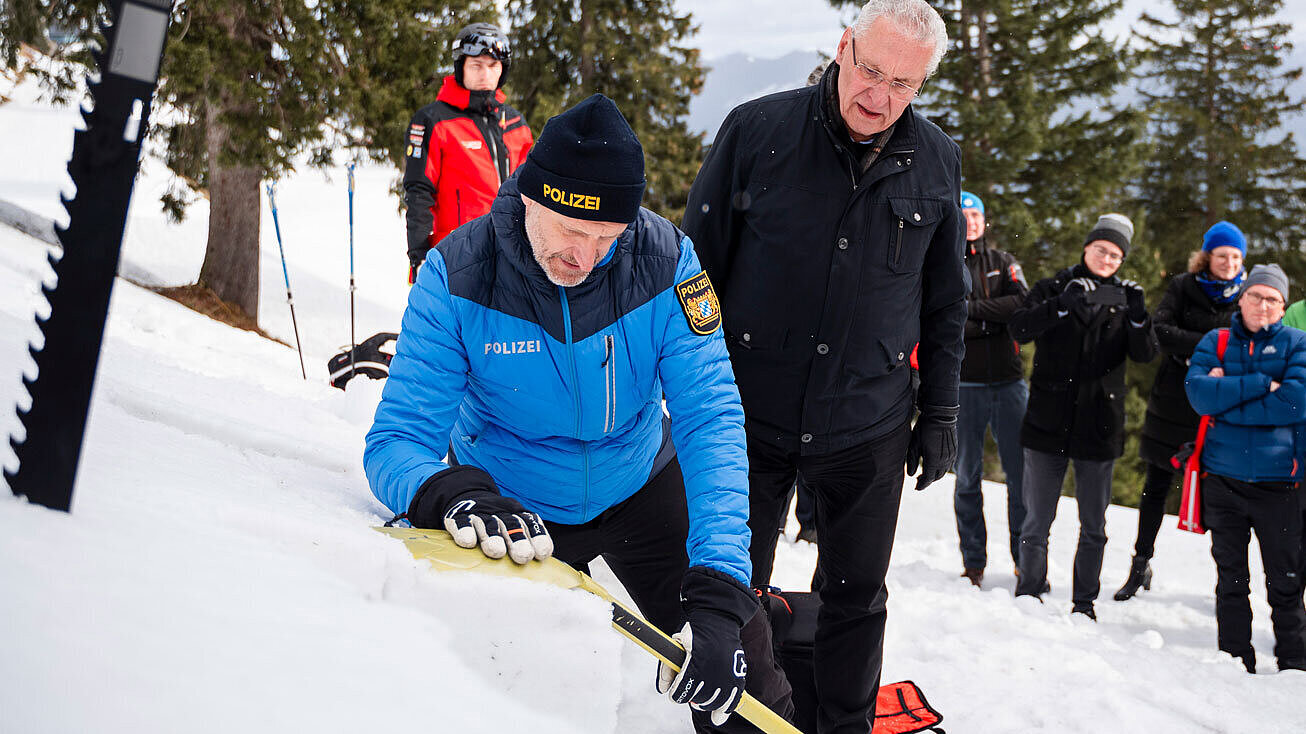 Innenminister Herrmann und Einsatzkräfte, u.a. ein Polizist, mit Lawinenschaufeln im Schnee