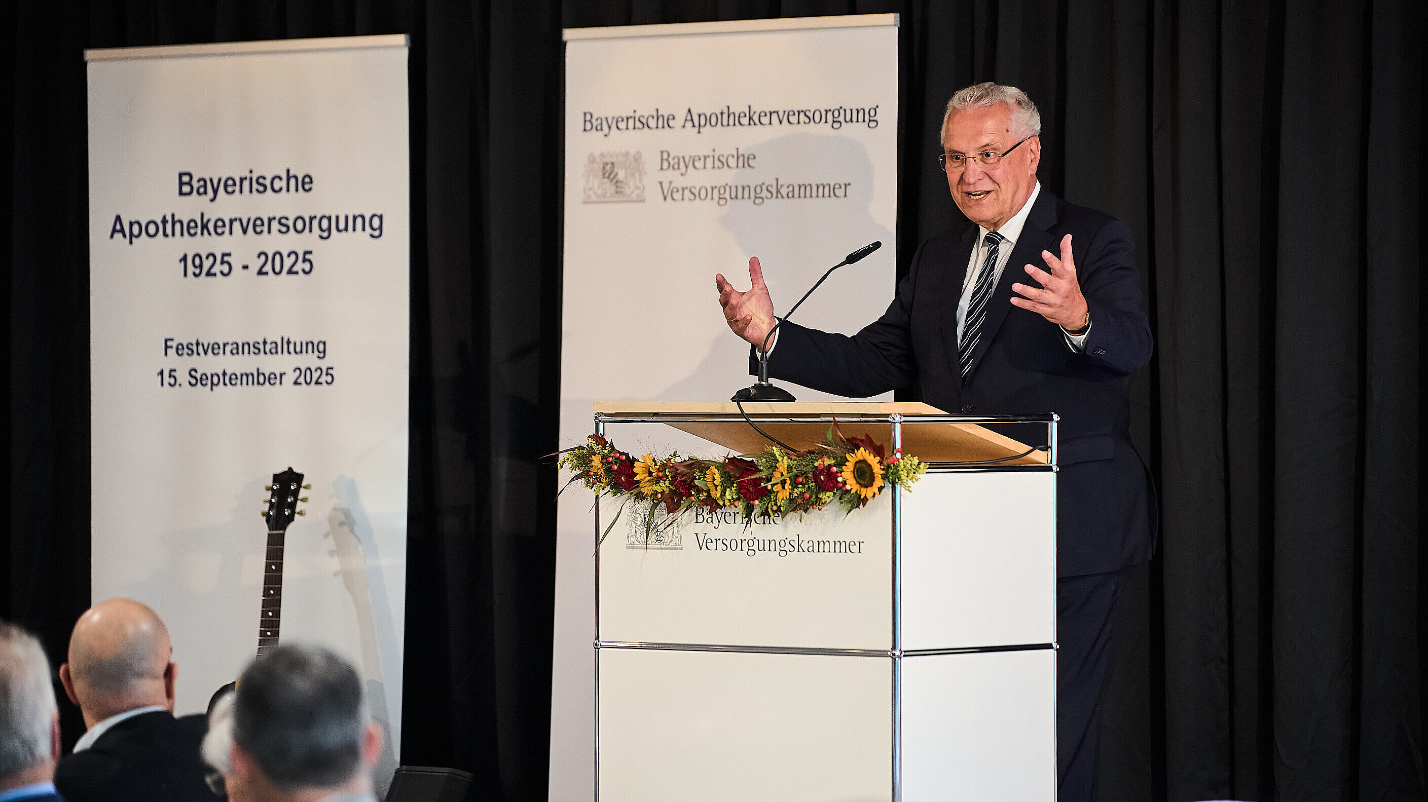 Innenminister Herrmann gestikulierend am Rednerpult, dahinter Rollups mit Bayerischer Apothekerversorgung, im Vordergrund Publikum