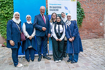 Gruppenbild Innenminister Herrmann mit Neubürgerinnen vor der Pressewand in Nürnberg