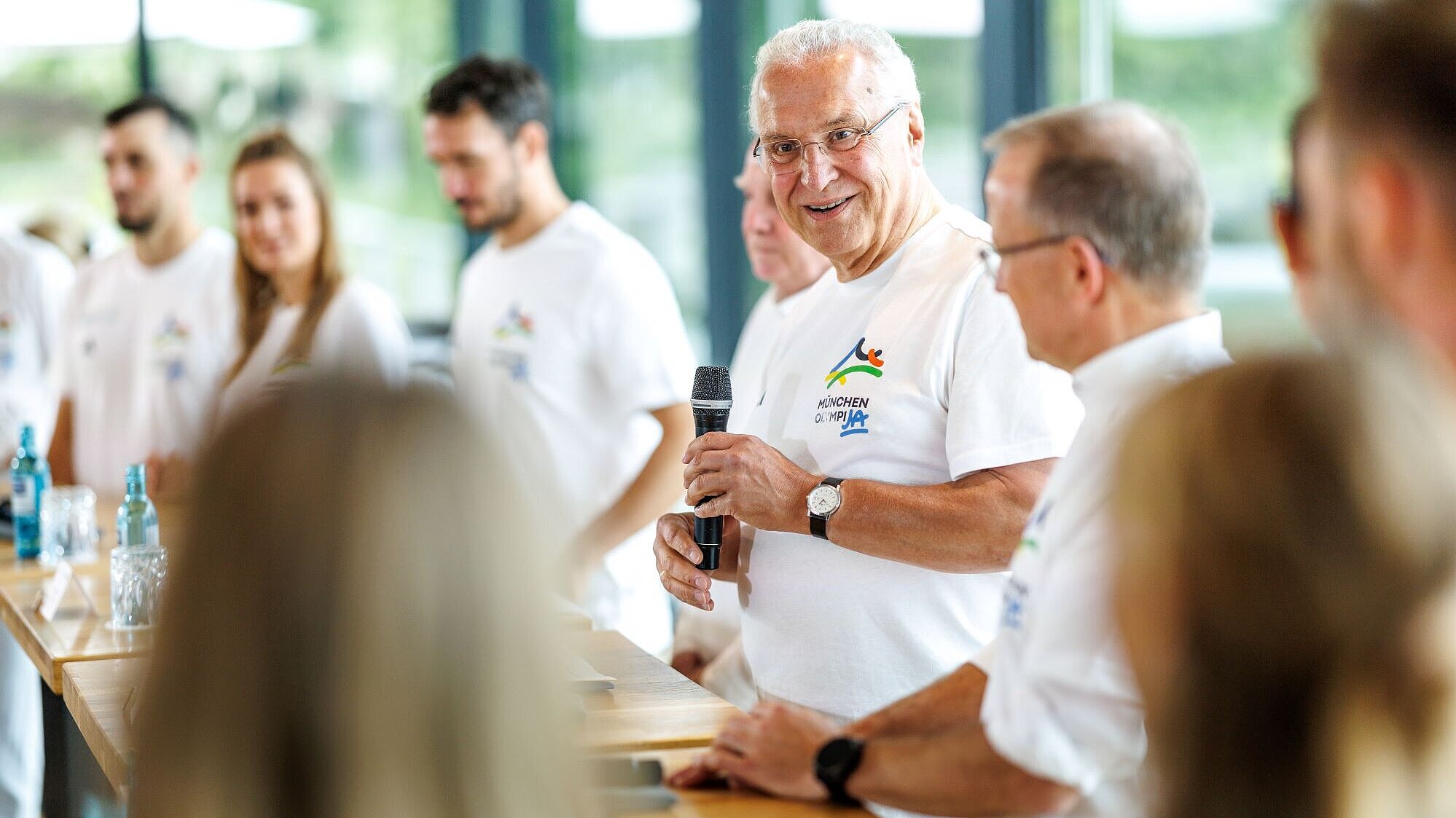 Auf dem Bild ist Innen- und Sportminister bei seiner Rede während der Pressekonferenz zu sehen. Neben ihm zahlreiche Sportlerinnen und Sportler sowie BLSV-Präsident Jörg Ammon.