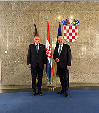 Innenminister Joachim Herrmann (rechts im Bild) trifft kroatischen Innenminister Dr. Davor Božinović (links im Bild). Sie stehen vor einem Fahnenset mit Blick zur Kamera