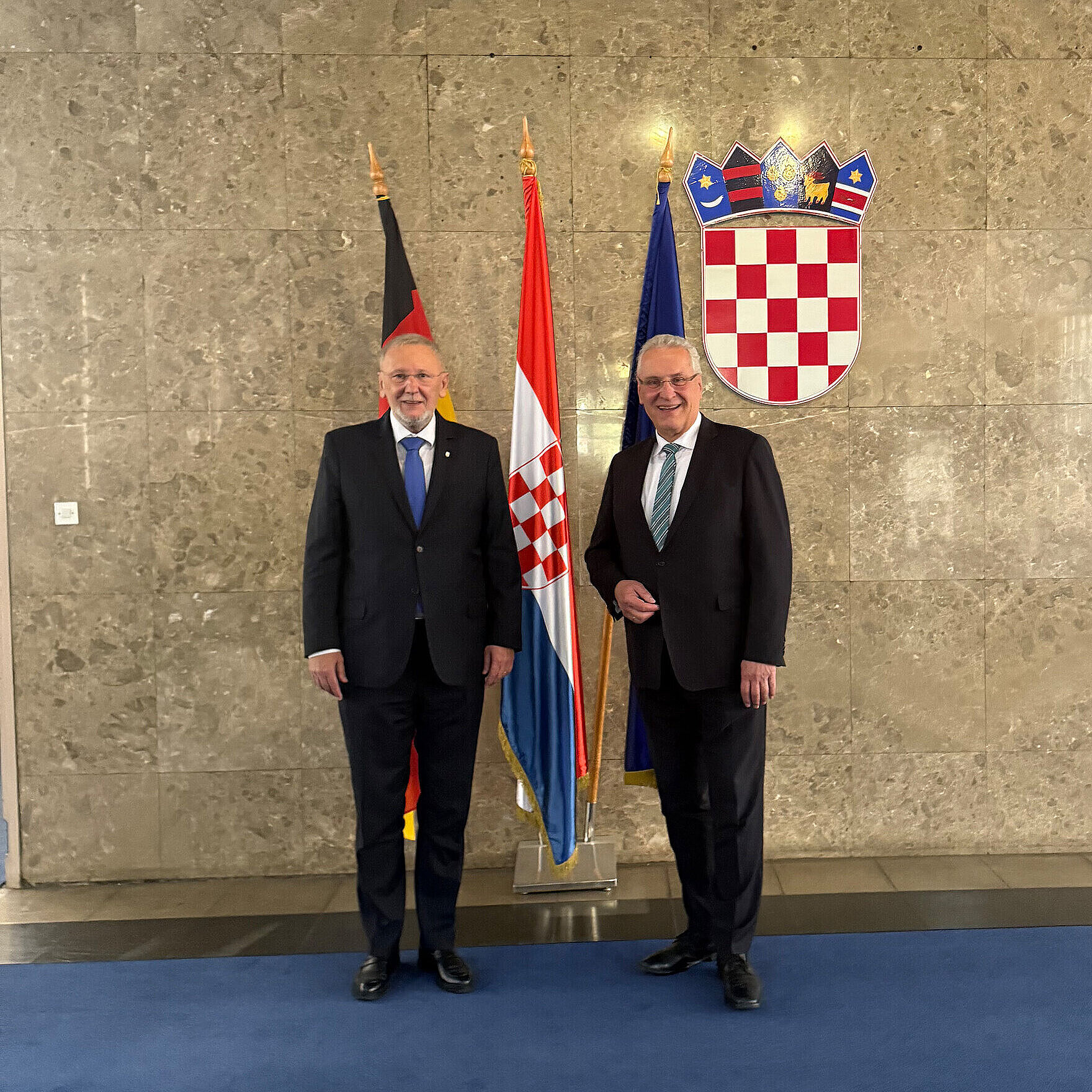 Innenminister Joachim Herrmann (rechts im Bild) trifft kroatischen Innenminister Dr. Davor Božinović (links im Bild). Sie stehen vor einem Fahnenset mit Blick zur Kamera