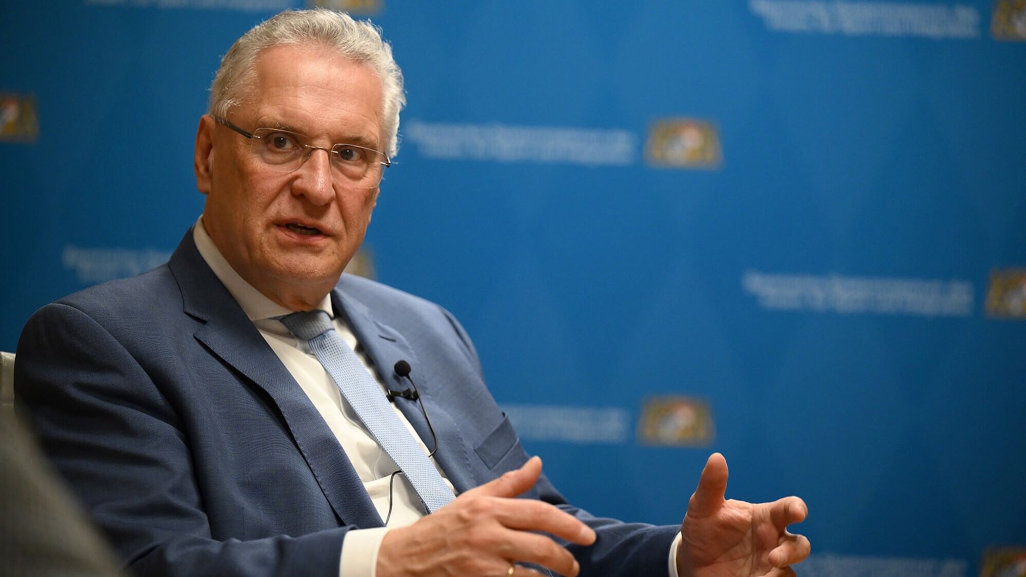 Auf dem Bild ist Innenminister Joachim Herrmann zu sehen, wie er in einer Gesprächsrunde diskutiert. Hinter ihm ist eine Zipperwand des Innenministeriums aufgebaut.