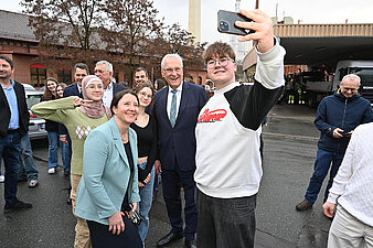 Ein Mann macht ein Selfie mit einer Gruppe von Freunden, alle lächeln und posieren fröhlich für die Kamera.