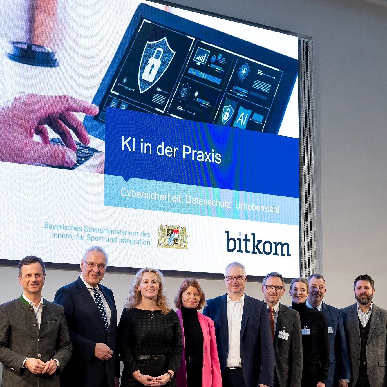 Gruppenfoto vor Präsentationsleinwand "KI in der Praxis" mit Innenminister Herrmann und weitere Akteure der Veranstaltung