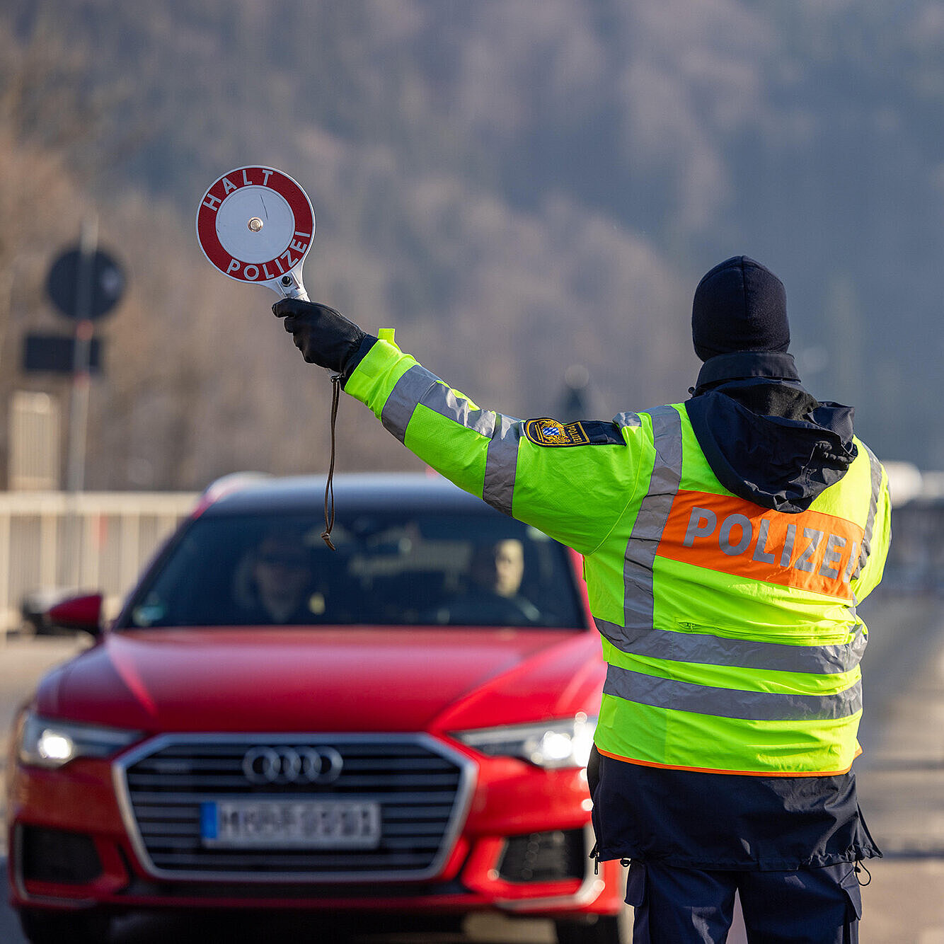Polizisten kontrollieren mehrere Fahrzeuge bei einer Straßenkontrolle; Beamte in gelben Warnwesten sprechen mit den Fahrerinnen und Fahrern.