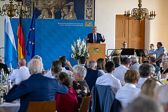 Publikum von hinten und Innenminister Herrmann auf der Bühne am Rednerpult