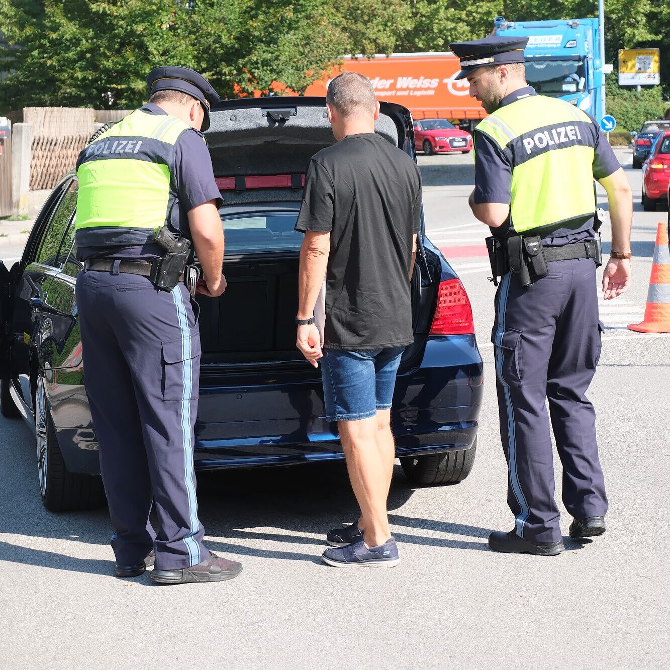 Zwei Polizisten lassen sich von einem Fahrer den Kofferraum zeigen