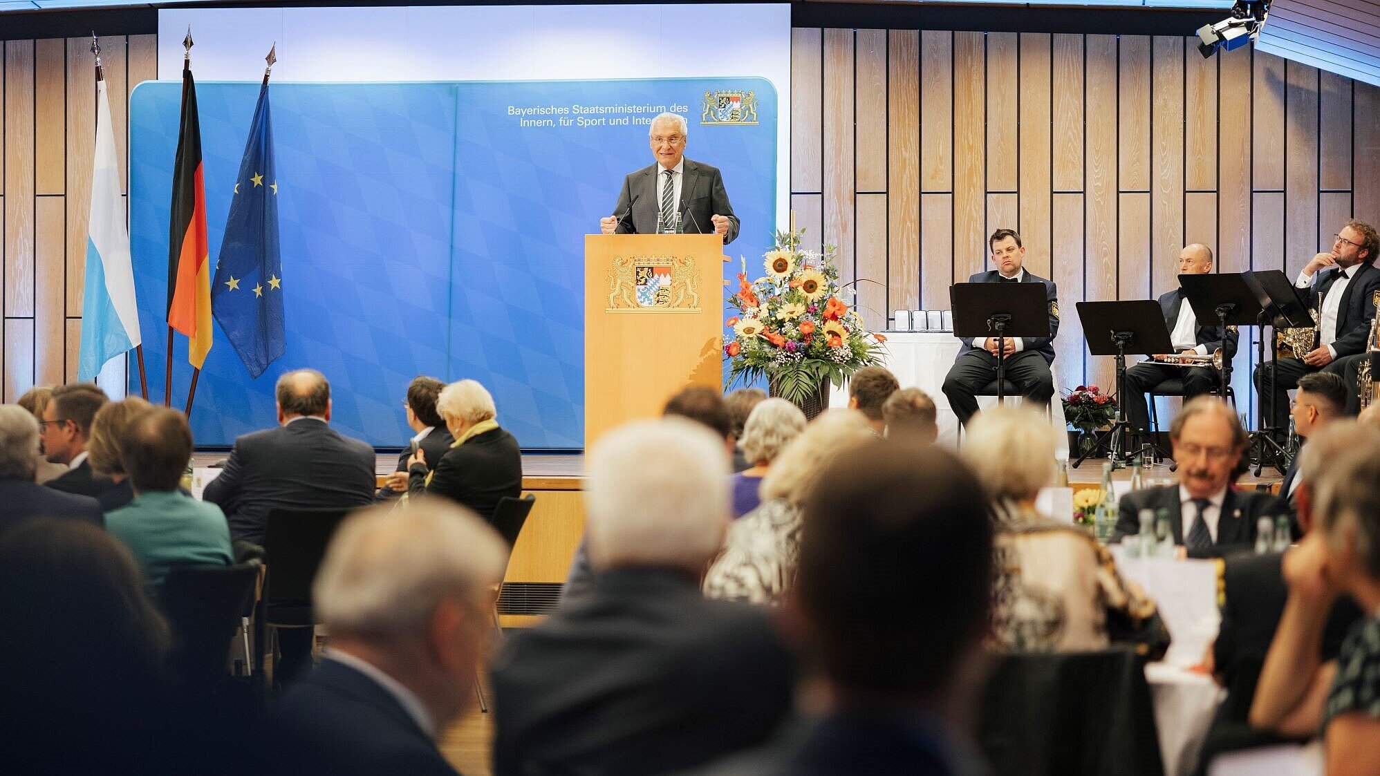 Auf dem Bild ist Innenminister Joachim Herrmann bei seiner Rede anlässlich der Ordensaushändigung am 30. Juli 2025 in Erlangen zu sehen. Vor ihm sieht man mehrere Gäste sitzen.