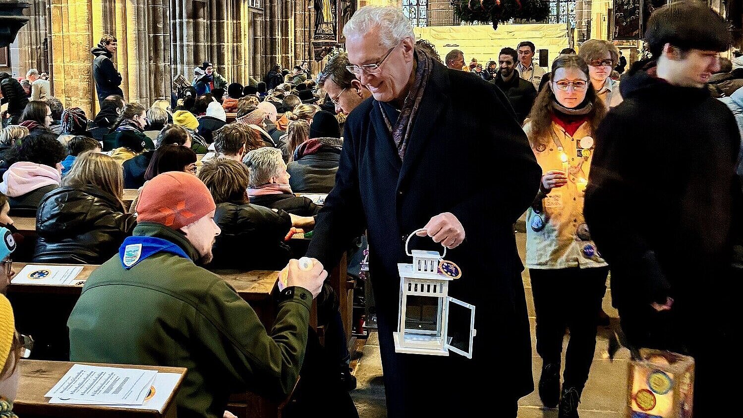 Innenminister Joachim Herrmann teilt das Friedenslicht weiter, hinter ihm die Kulisse der Lorenzkirche.