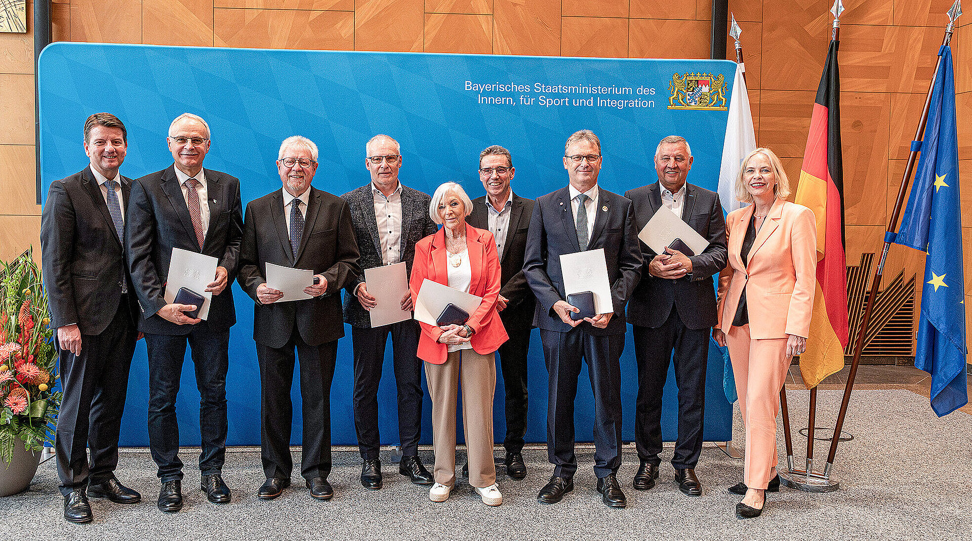 Gruppenbild vor blauer Pressewand von links nach rechts Staatssekretär Sandro Kirchner im dunklen Anzug mit den Preisträgern und ganz rechts Frau Regierungspräsidentin von Unterfranken