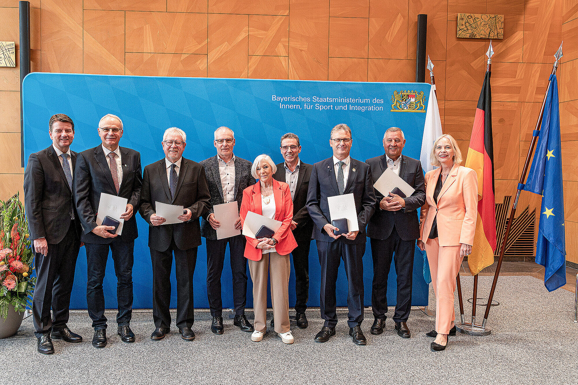 Gruppenbild vor blauer Pressewand von links nach rechts Staatssekretär Sandro Kirchner im dunklen Anzug mit den Preisträgern und ganz rechts Frau Regierungspräsidentin von Unterfranken