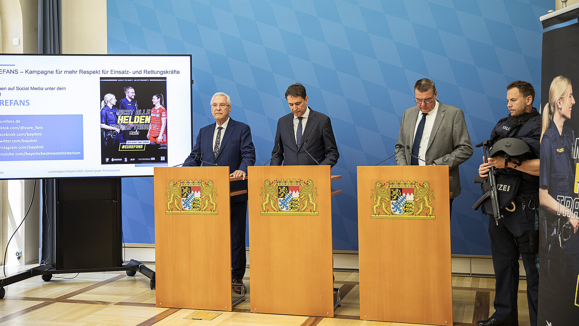 Herrmann, Eisenreich und Lintl an Rednerpulten, rechts daneben ein Polizist mit Schutzausrüstung