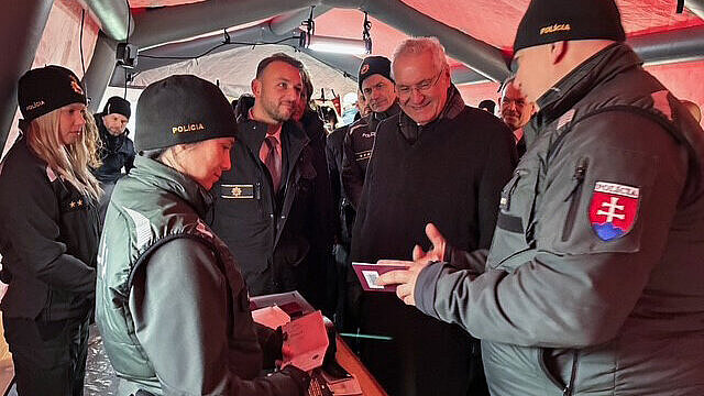 Innenminister Herrmann zwischen mehreren Leuten von der Polizei in Zelt, lässt sich etwas zeigen