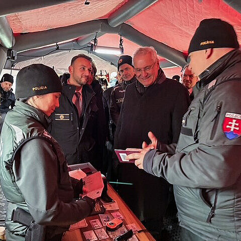 Innenminister Herrmann zwischen mehreren Leuten von der Polizei in Zelt, lässt sich etwas zeigen