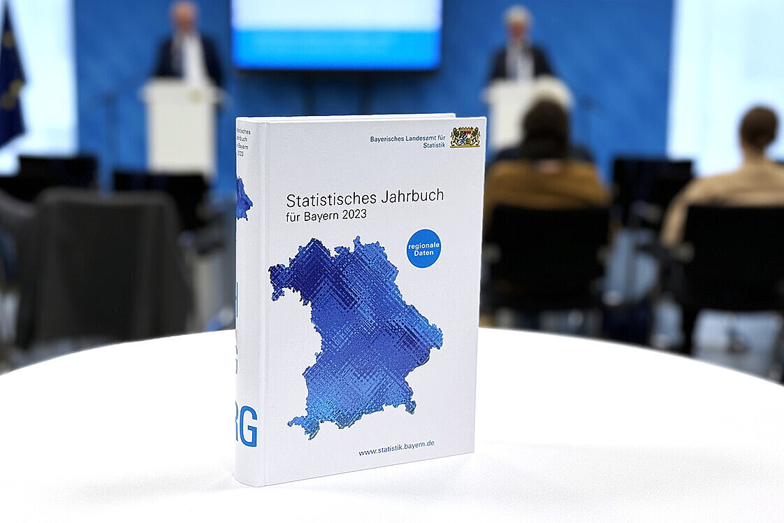 Statistisches Jahrbuch für Bayern 2023 auf einem Tisch stehend, im Hintergrund die Pressekonferenz