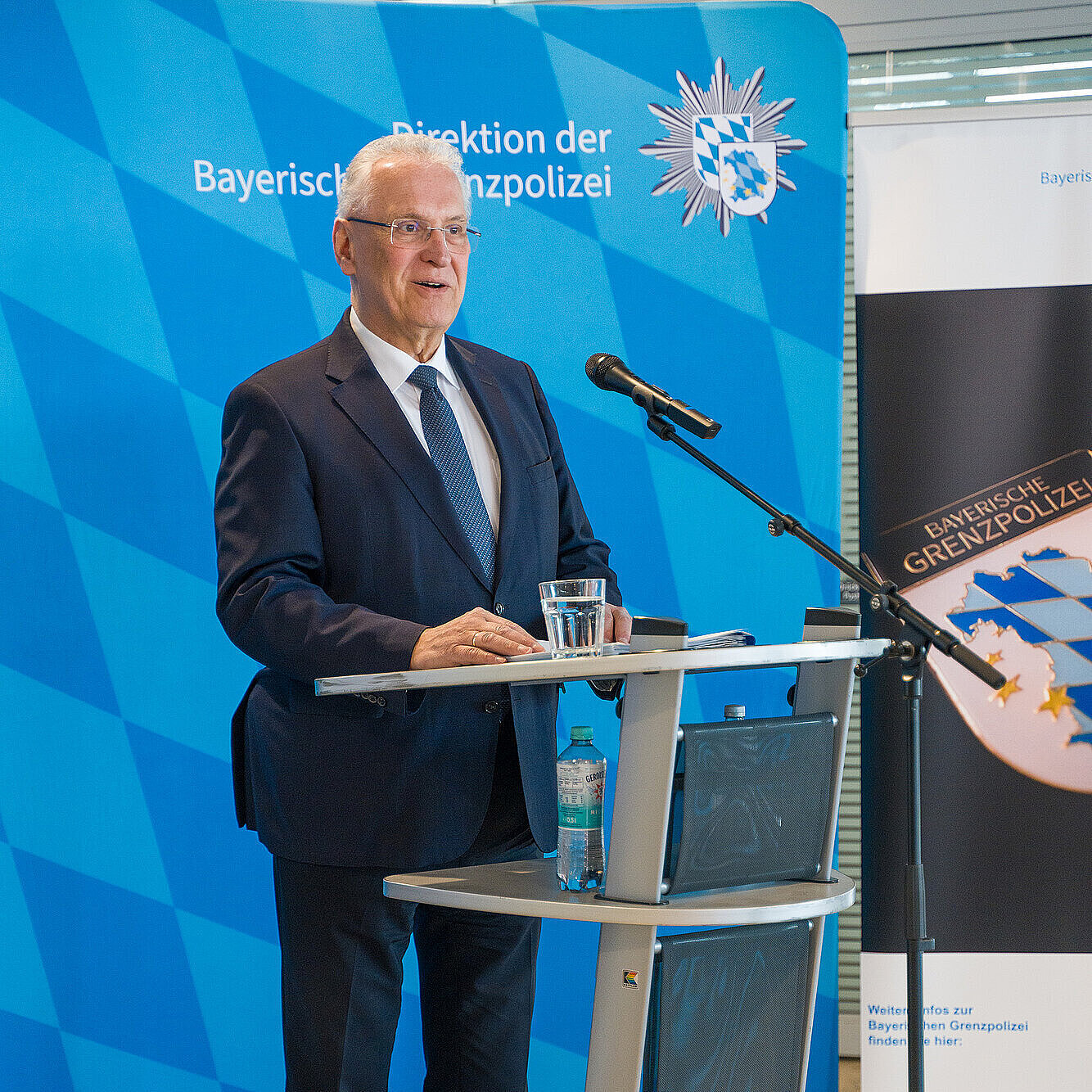 Ein Mann am Rednerpult im Hintergrund steht eine blaue Pressewand mit dem Polizei-Logo.