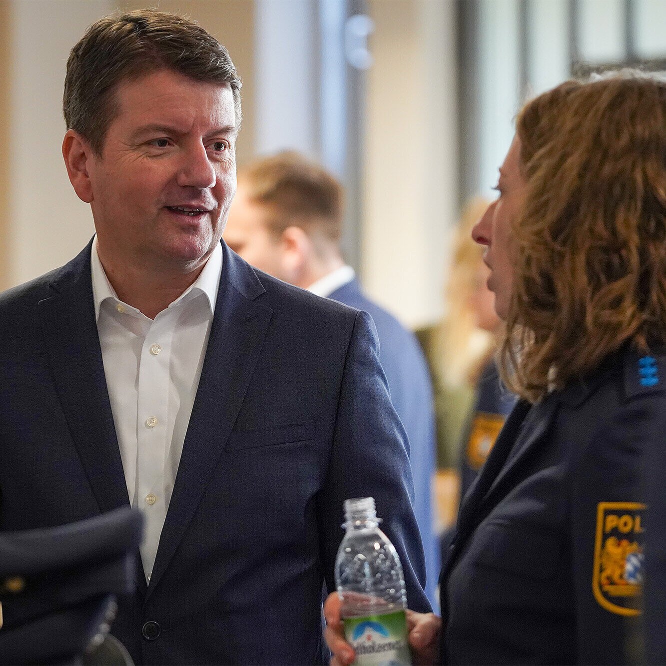 Ein Mann im Anzug im Gespräch mit einer Frau in Uniform.