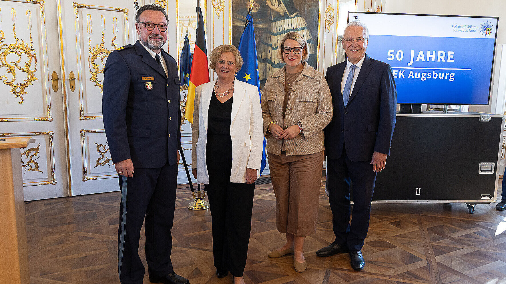 Gruppenfoto mit Innenminister Herrmann, Regierungspräsidentin von Schwaben Barbara Schretter und zwei weiteren in festlichem Saal mit Präsentation