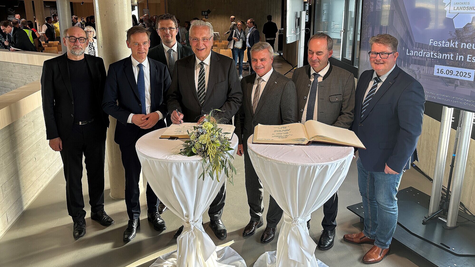 Innenminister Joachim Herrmann in der Gruppe mit weiteren Personen vor Stehtischen und einer Präsentation in festlichem Raum
