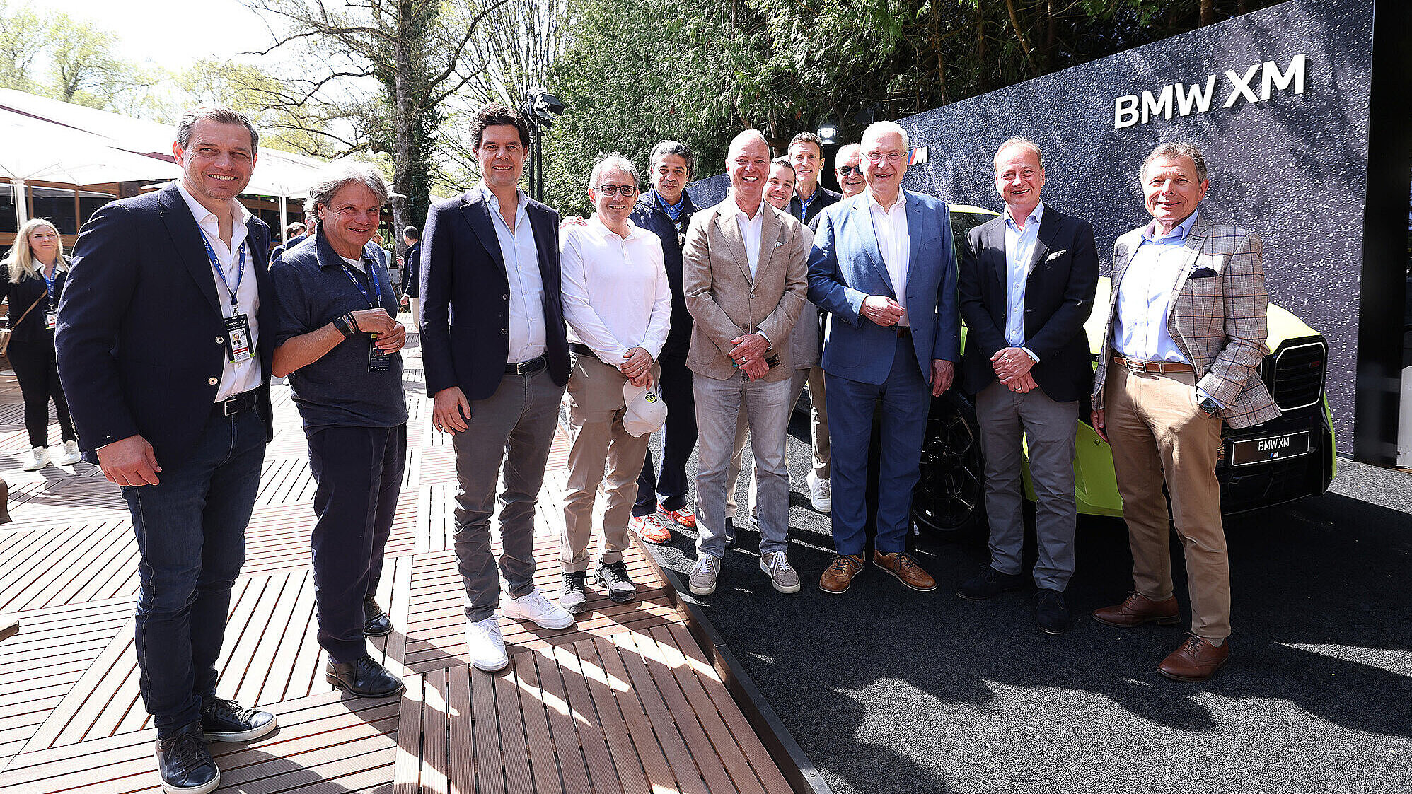 Gruppenfoto von rund zehn Personen beim BMW Open im Freien vor einem BMW XM Fahrzeug und einer dunklen Sponsorenwand mit BMW XM Schriftzug.