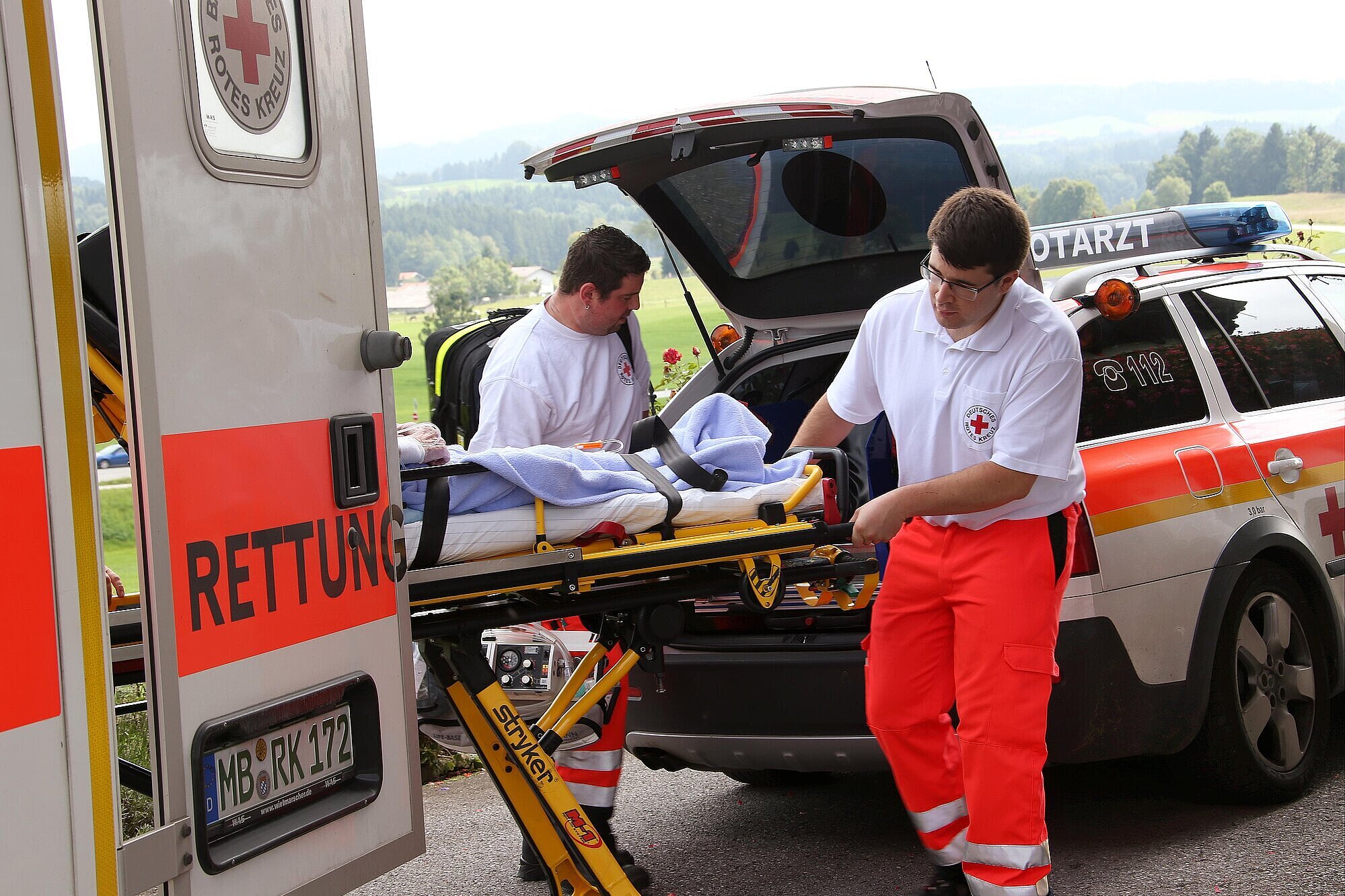 Zwei Rettungsassistenten des BRK die eine Trage mit Patienten in einen Notarztwagen hieven
