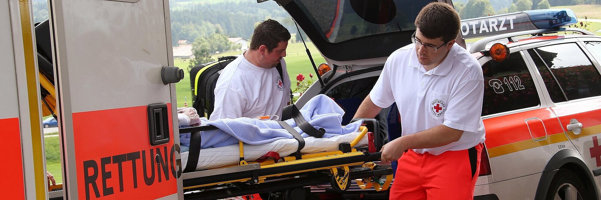 Zwei Rettungsassistenten des BRK die eine Trage mit Patienten in einen Notarztwagen hieven