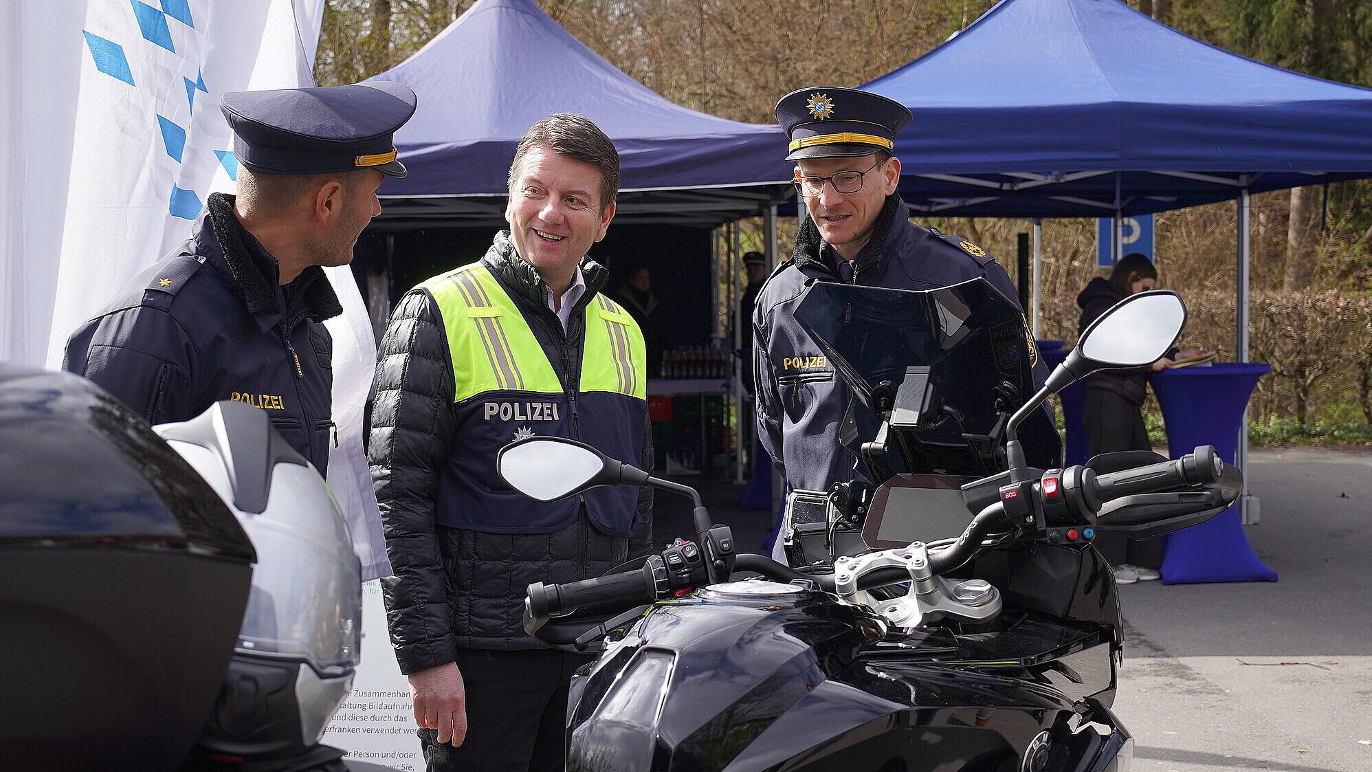 Drei Männer im Gespräch, zwei davon in Polizeiuniform, im Vordergrund ein Motorrad