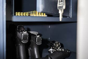 Blick in einen Waffenschrank mit drei Polizeipistolen und Munition im oberen Fach, abschließbar mit Schlüssel