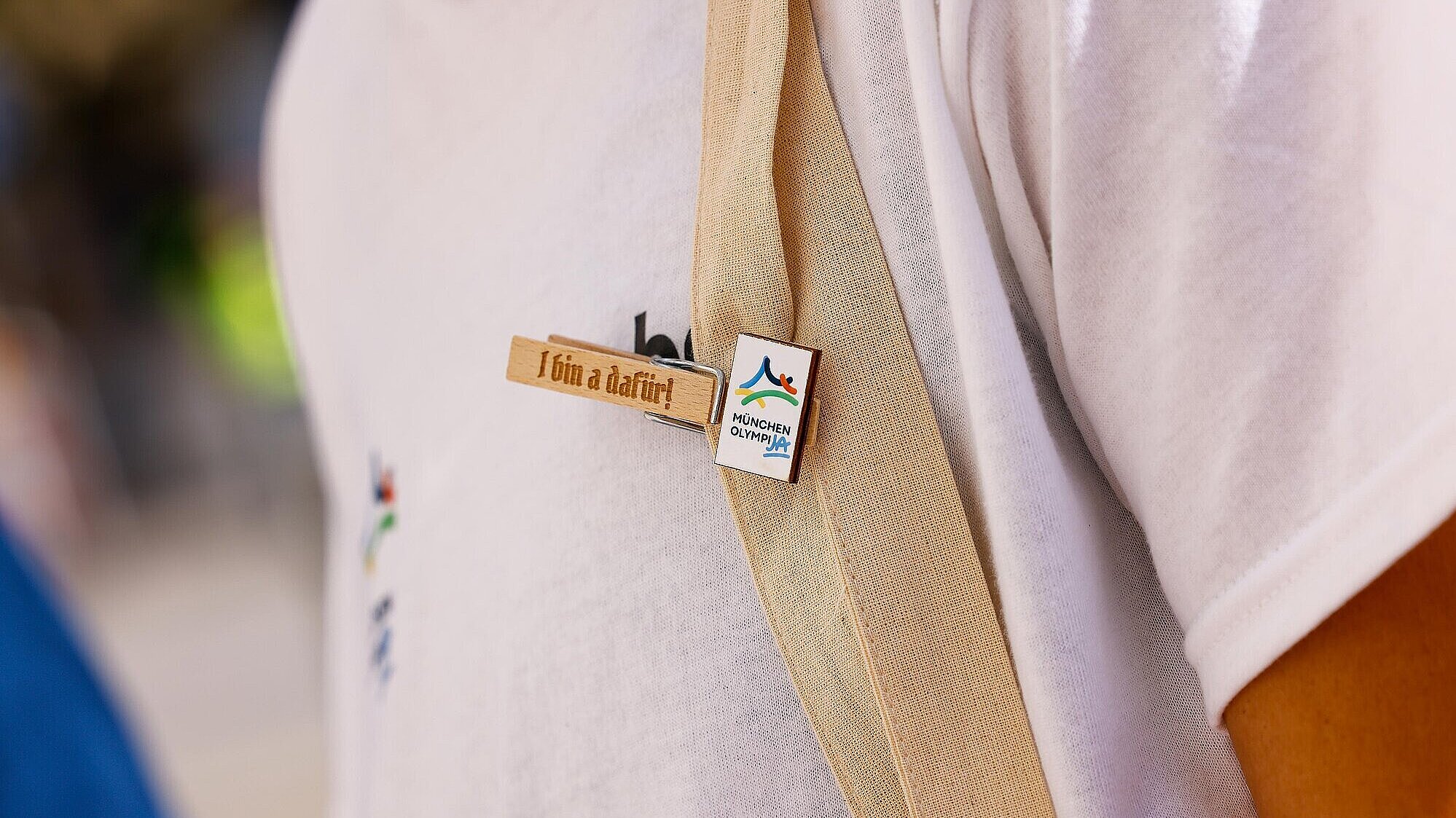 Detailaufnahme von einer Wäscheklammer an einer Person mit der Aufschrift "I bin a dafür" und dem OlympiJA-Logo