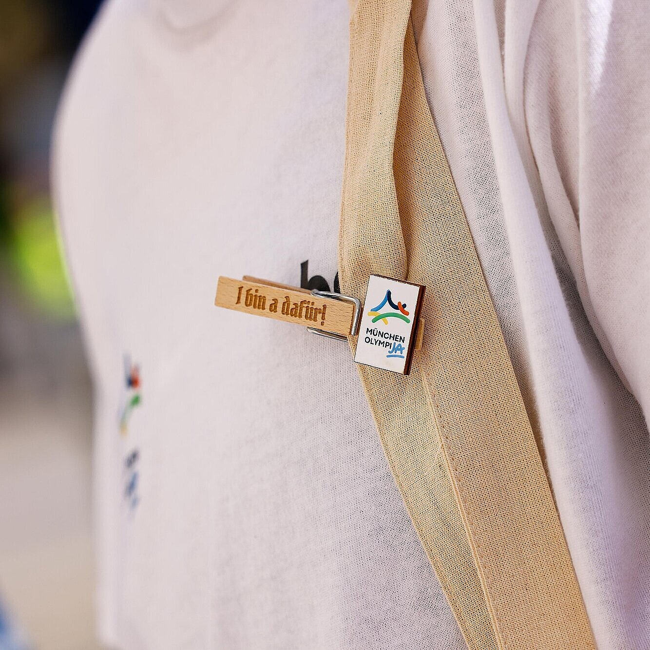 Detailaufnahme von einer Wäscheklammer an einer Person mit der Aufschrift "I bin a dafür" und dem OlympiJA-Logo