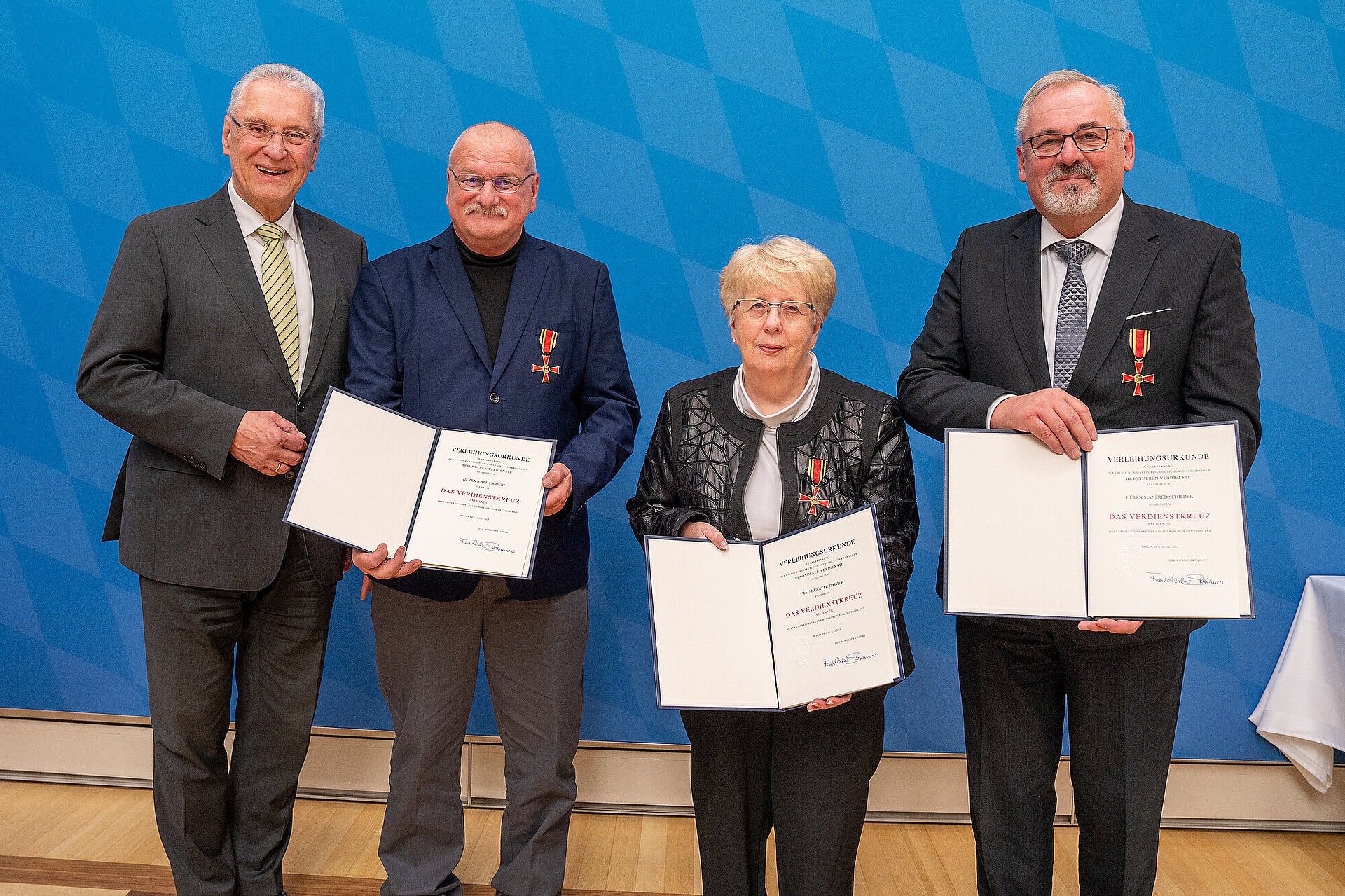 Innenminister Herrmann mit den drei Geehrten mit ihren Urkunden und dem Verdienstkreuz.