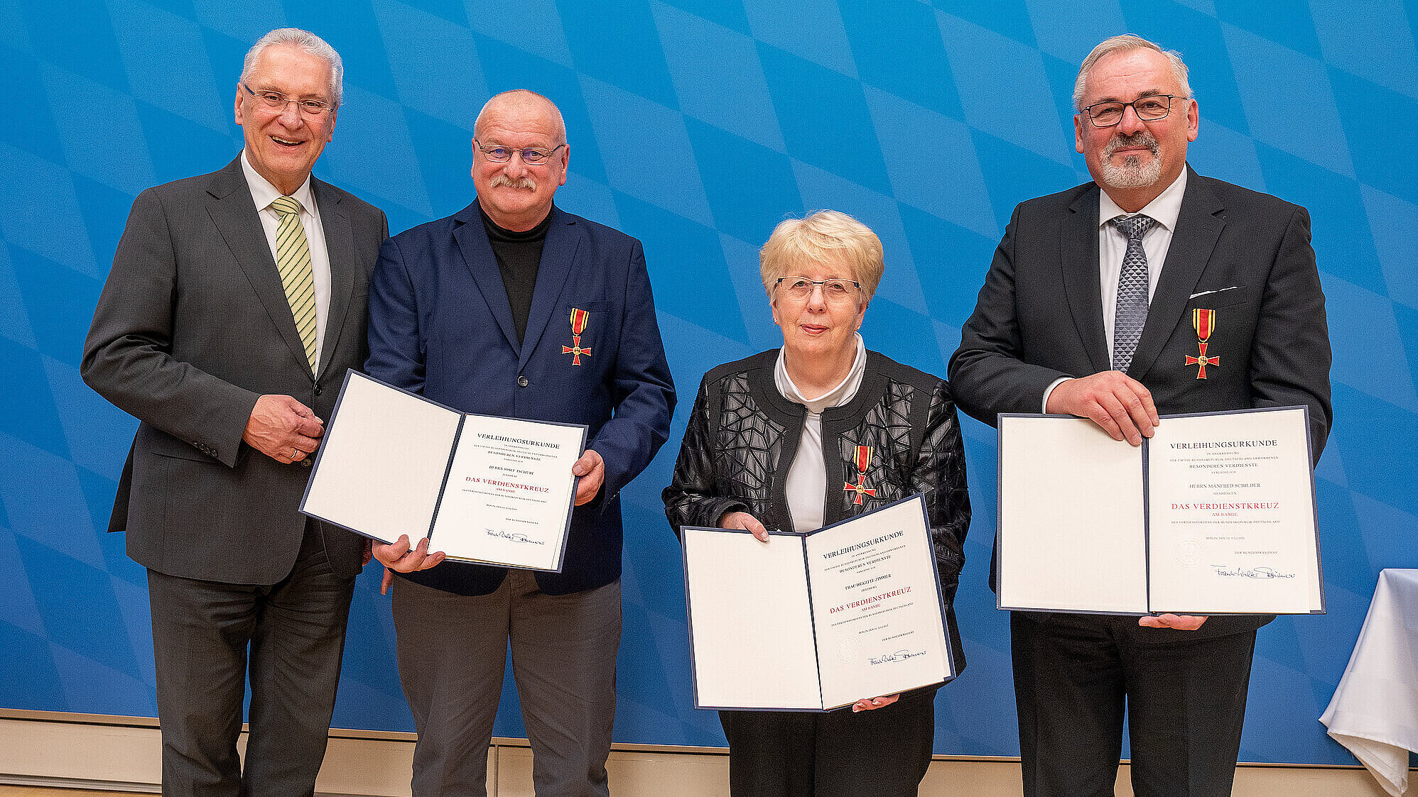 Innenminister Herrmann mit den drei Geehrten mit ihren Urkunden und dem Verdienstkreuz.