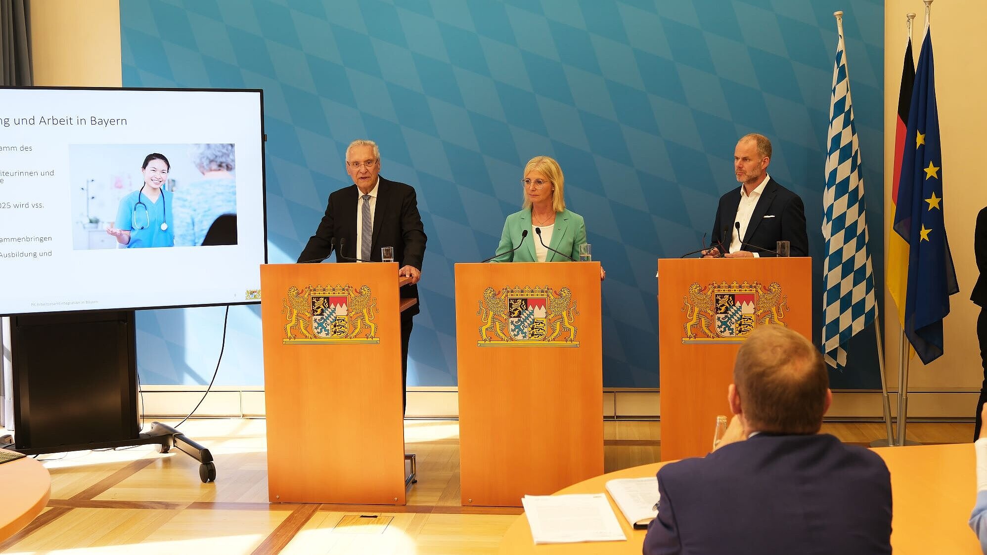 Auf dem Bild sind Innenminister Joachim Herrmann, Arbeitsministerin Ulrike Scharf sowie Dr. Markus Schmitz (Agentur für Arbeit) bei ihrer gemeinsamen Pressekonferenz zu sehen.