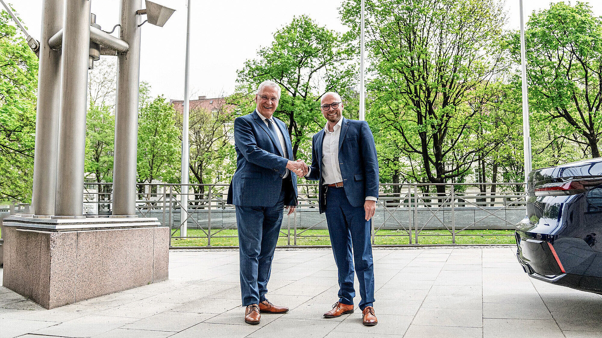 Herrmann und Mehring schütteln sich die Hand vor Fahnenmasten vor Staatskanzlei