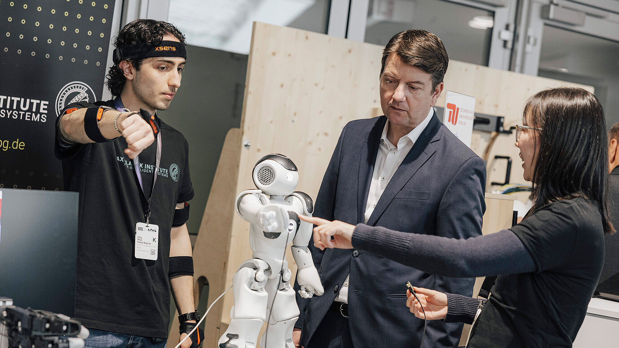 auf dem Bild: Staatssekretär Kirchner bei seinem Messerundgang im Gespräch mit eine Entwicklern, vor einem keinen Roboter