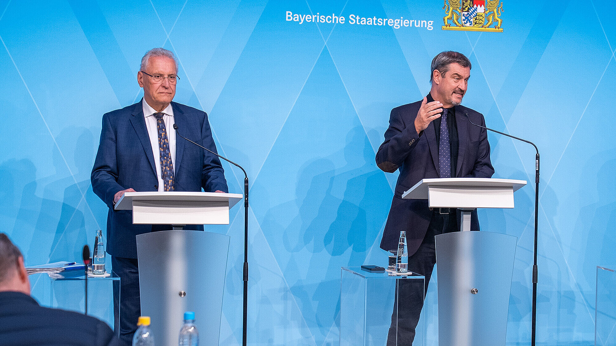 Innenminister Joachim Herrmann links im Bild und Ministerpräsident Dr. Markus Söder rechts im Bild stehen vor einer blauen Pressewand mit dem Logo Bayerische Staatsregierung an Rednerpulten mit Blick nach vorn.