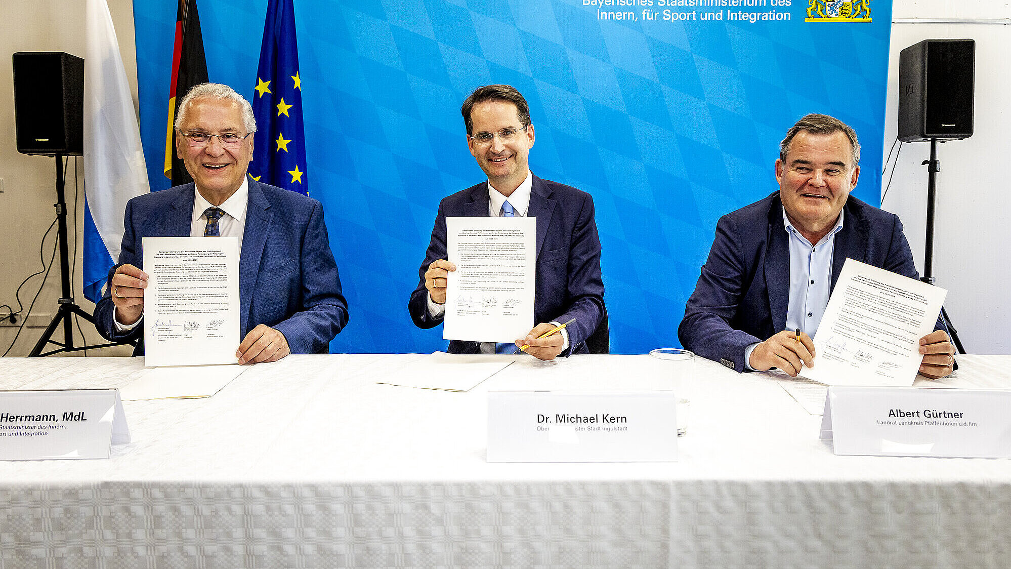 Herrmann, Kern und Gürtner am Tisch, halten drei unterzeichnete Papiere hoch, dahinter Pressewand