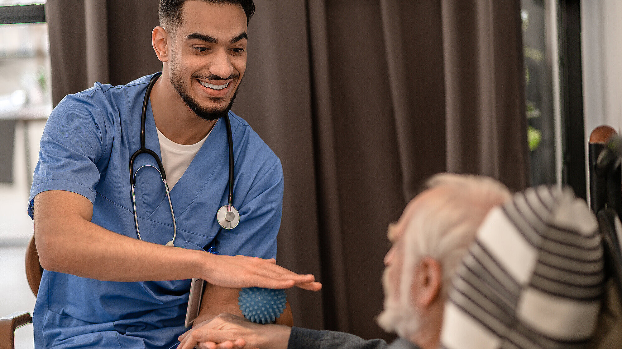 Lächelnder, freundlicher Physiotherapeut führt eine Physiotherapie-Sitzung zu Hause durch.