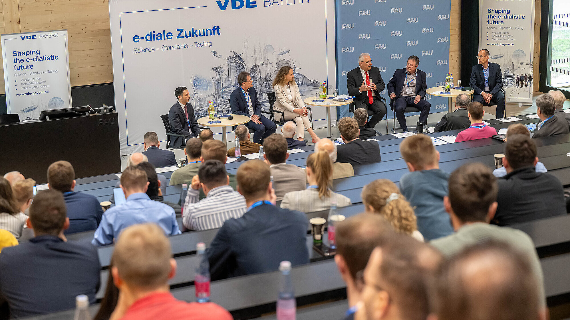 Ein Lehrsaal mit aufmerksamen Zuhörerinnen und Zuhörern hören mehreren Personen bei einer Podiumsdiskussion zu.