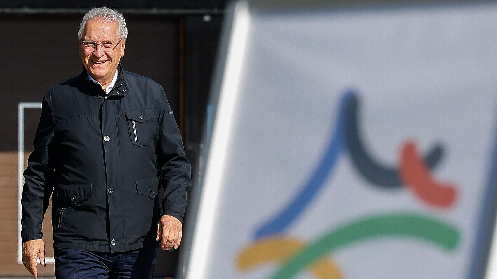 Staatsminister Joachim Herrmann gehend von vorne, im unscharfen Vordergrund Aufsteller mit OlympiJA-Logo