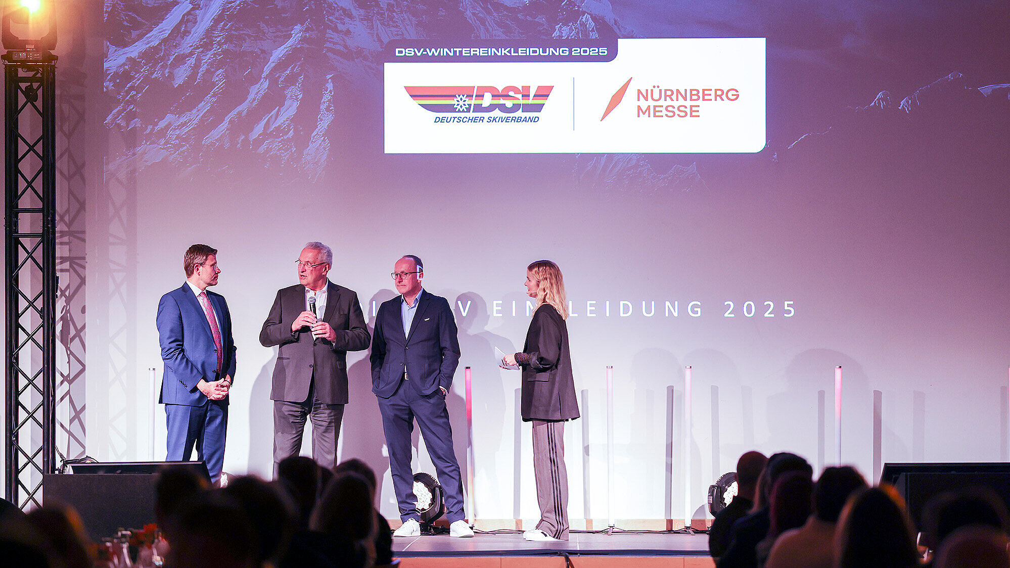 Innenminister Joachim Herrmann 2.v.li.  steht auf einer Bühne und präsentieren bei einem Event vor einem Publikum.