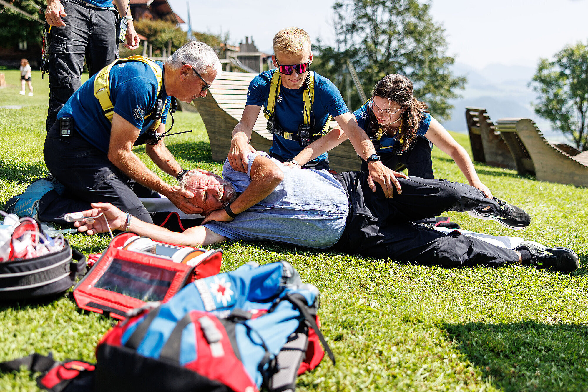 Sanitäter der Bergwacht bringen Verletzte Person auf einer Wiese in stabile Seitenlage