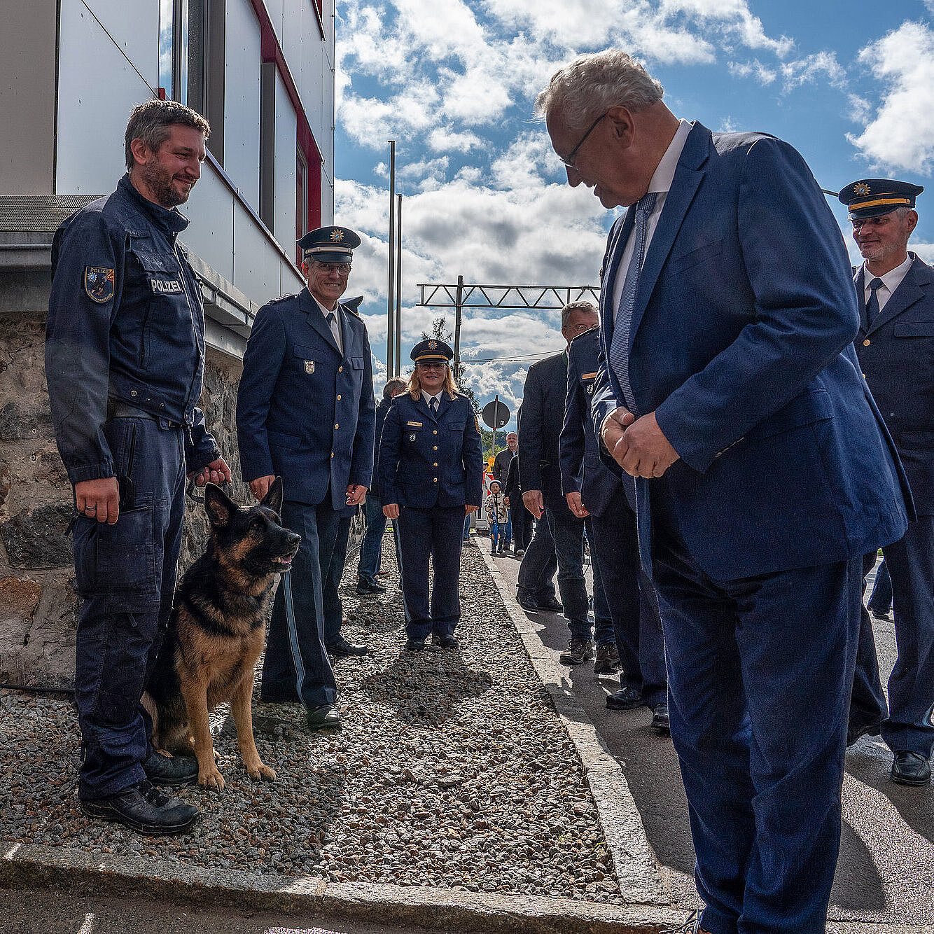 Innenminister Joachim Herrmann blickt zu einem Schäferhund neben Polizist, im Hintergrund weitere Polizisten