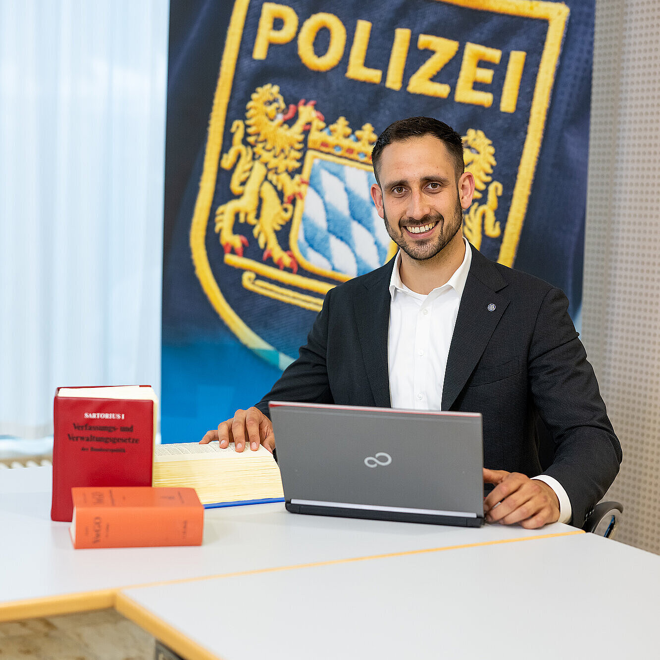Jurist mit Laptop und Gesetzesbänden vor Polizei-Rollup