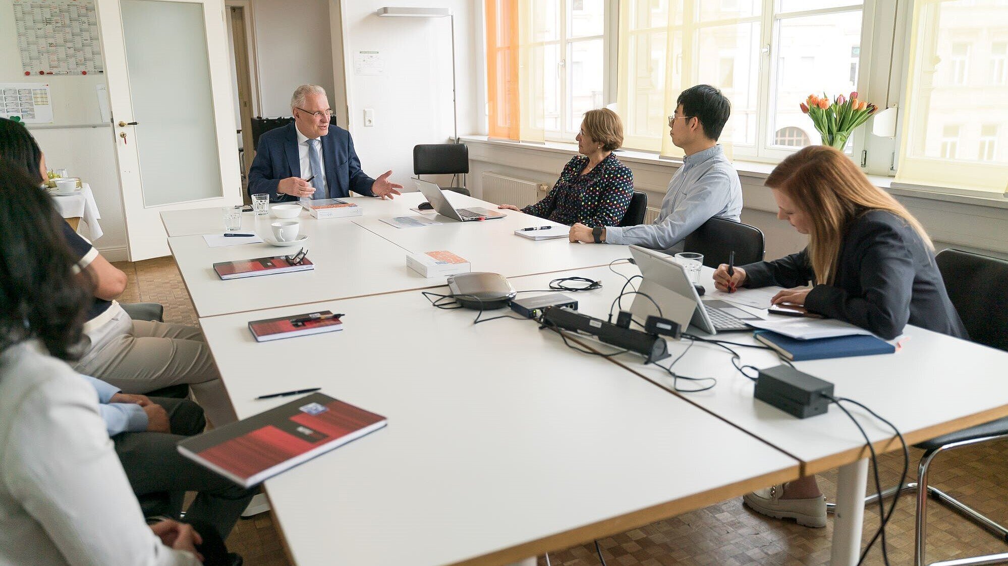 Auf dem Bild ist Innenminister Joachim Herrmann mit Mitarbeiterinnen und Mitarbeitern der Firmen HMG Systems Engineering GmbH und PGXperts GmbH an einem Besprechungstisch zu sehen.