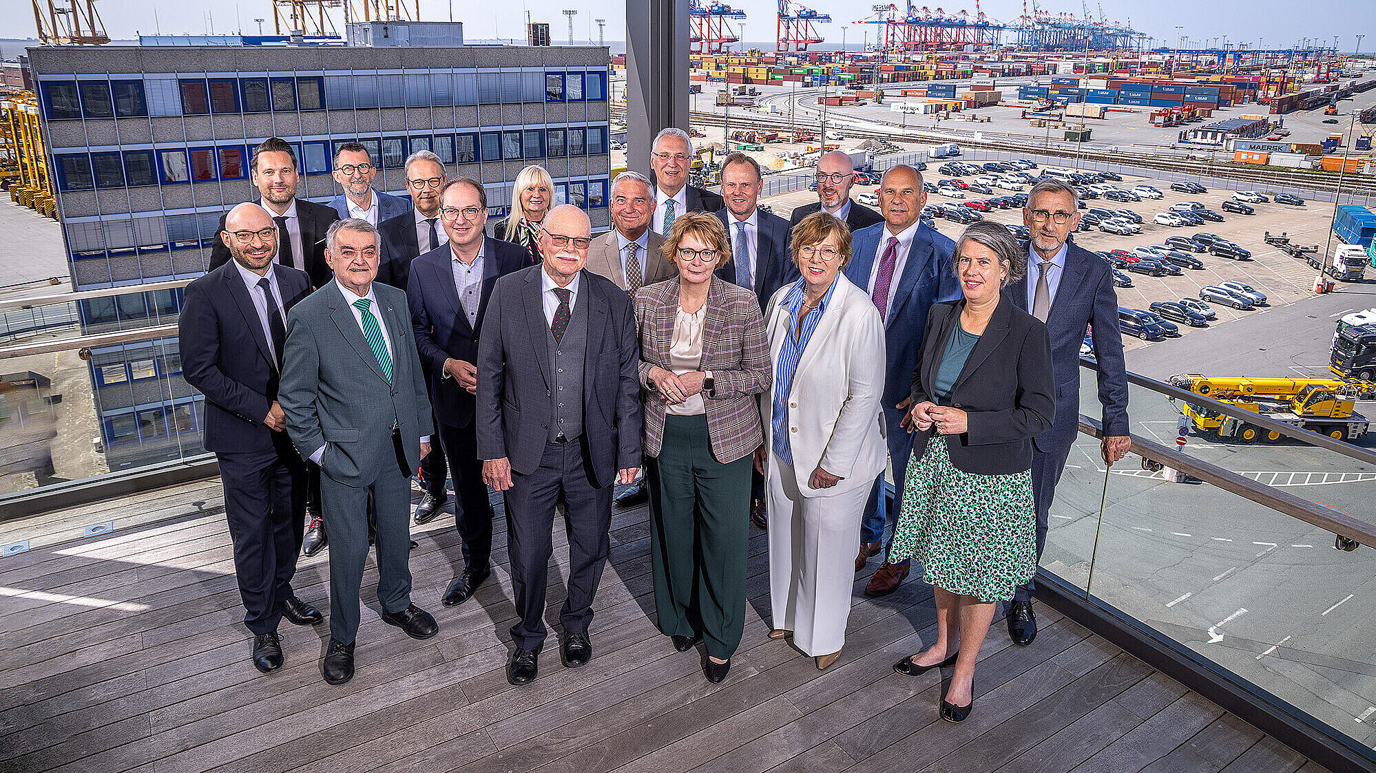 Gruppenfoto der Teilnehmer der IMK Personen in Businesskleidung auf einem Balkon mit Blick auf einen Containerhafen. Im Hintergrund sind zahlreiche Container, Kräne und geparkte Autos zu sehen. Die Personen stehen eng beieinander und lächeln in die Kamera. 