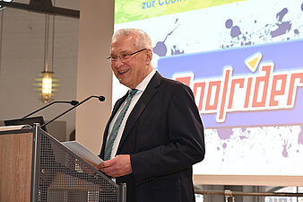 Ein Mann im Anzug und mit Krawatte steht an einem Rednerpult.