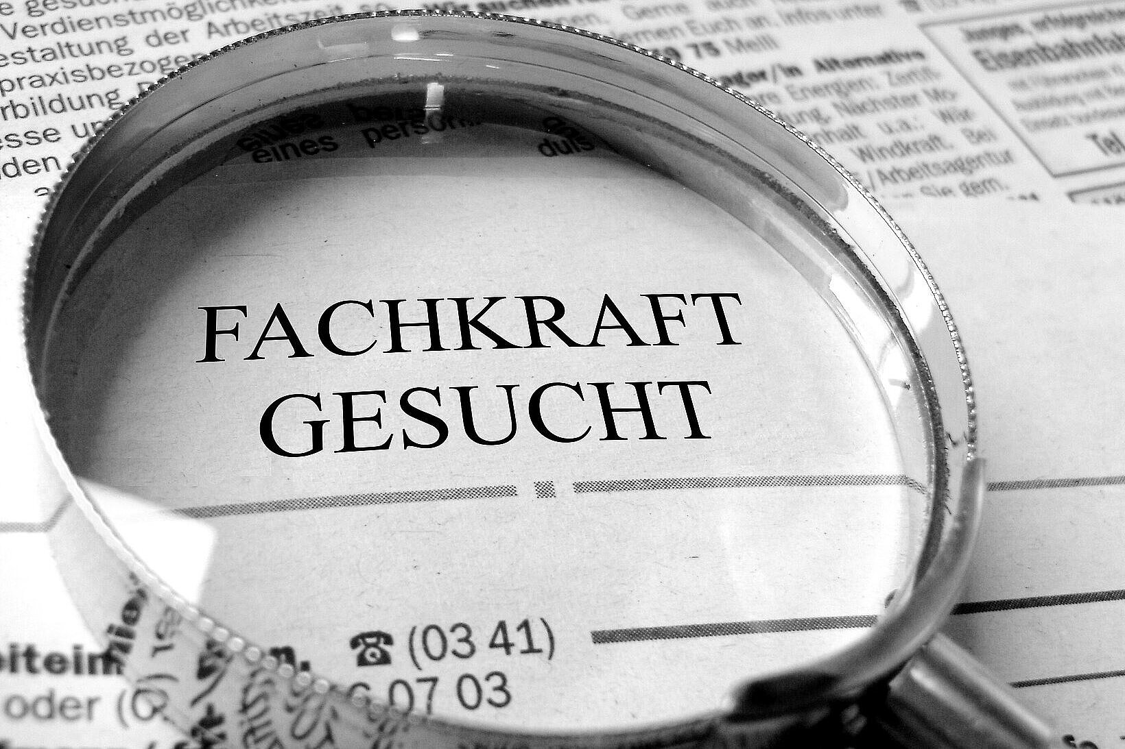 auf einer Zeitung liegt eine Lupe, der Schriftzug Fachkräfte gesucht scheint durch die Lupe 
