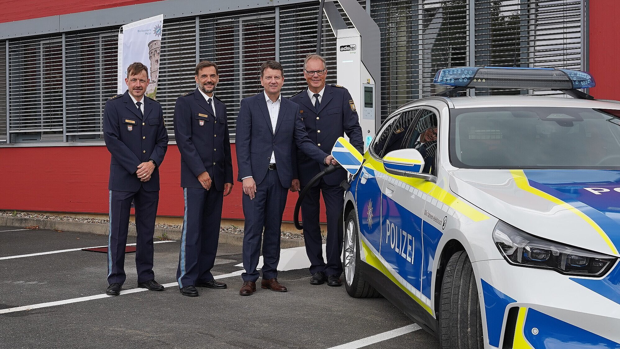 Auf dem Bild ist Innenstaatssekretär Sandro Kirchner mit Vertretern des Polizeipräsidiums Unterfranken zu sehen und einem Elektro-Streifenwagen.